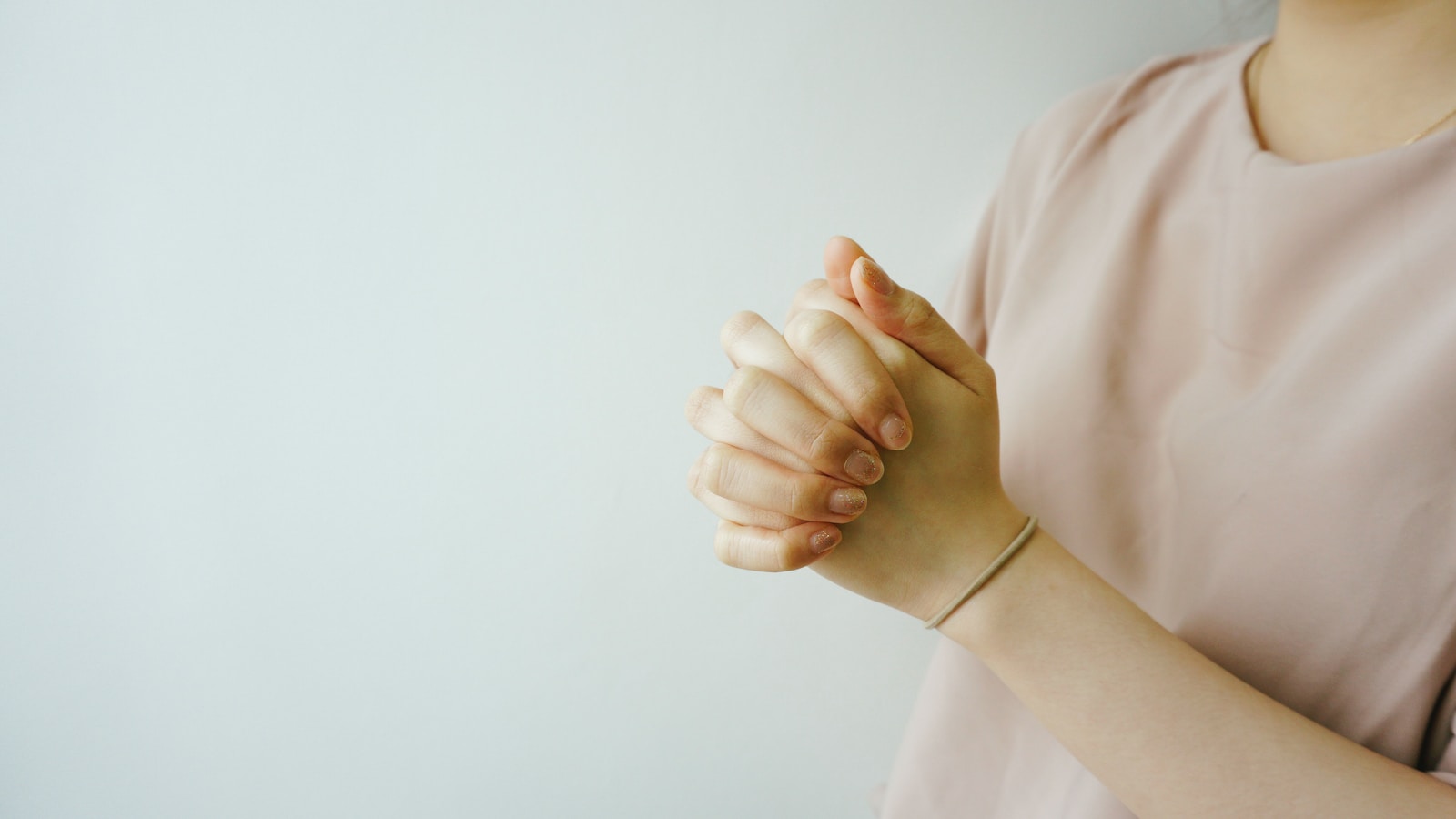 person wearing pink crew-neck shirt with hand clasped together